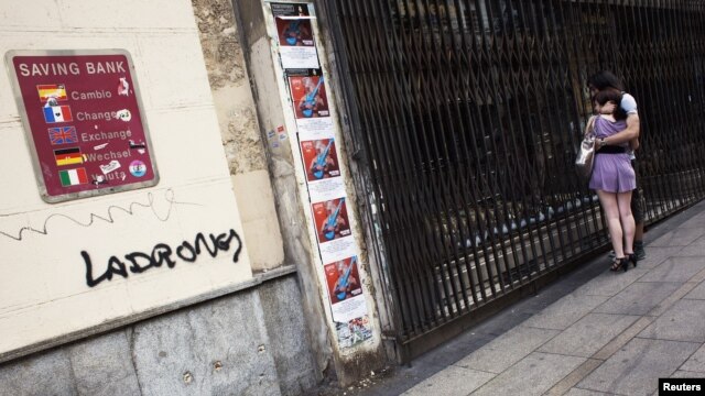 Par gleda izlog zatvorene trgovine pored zida sa kursnom listom i grafiom 'lopovi', Madrid, juni 2012.