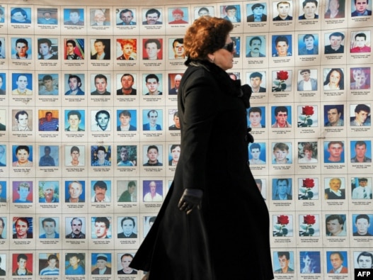 An woman walks past a wall in Pristina on January 25 of photos depicting people missing since the 1998-99 conflict in Kosovo.