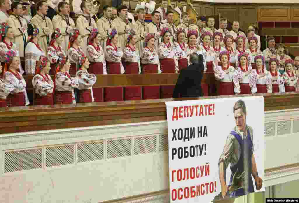 A choir sings during the ceremonial opening of a new session of parliament in Kyiv, Ukraine. The large poster urges deputies to "vote in person," a reference to so-called piano voting, in which deputies present in the chamber press electronic voting buttons for absent colleagues. (Reuters/Gleb Garanich)
