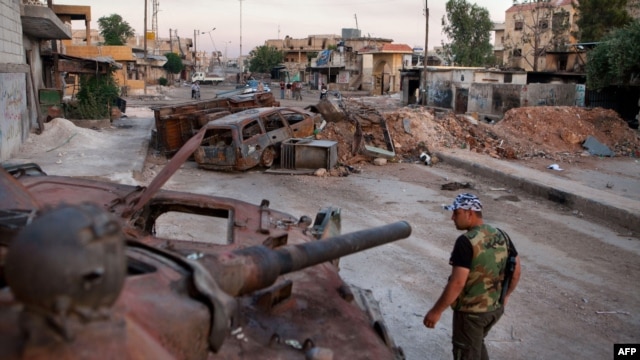 A member of the Free Syria Army walks past a destroyed Syrian forces tank in the town Atareb in northern Aleppo province.
