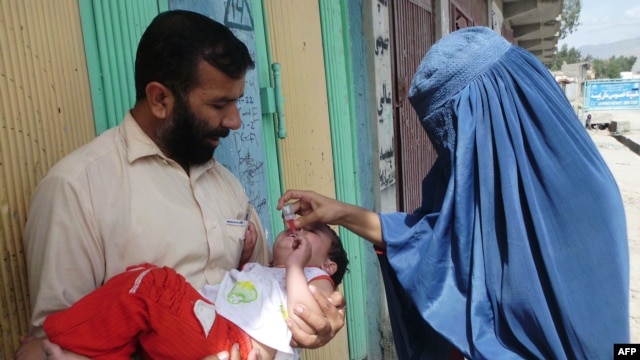 An Afghan health worker (right) administers a polio vaccination to a child on the second day of a vaccination campaign in Laghman province.