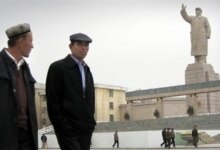 China -- Uyghur (Uighur) Muslims walk past a statue of Mao Zedong in the city of Kashgar, in Xinjiang region, 27Mar2005