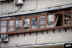 Мужчина выглядывает с балкона пострадавшего жилого дома, в который попал снаряд, 25 февраля 2022 года