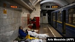 Qadın Kyivde sığınaq olaraq qullanılğan metro stantsiyasında otura, 2022 senesi martnıñ 2-si
