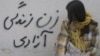 A young Iranian woman sits close to a wall with the slogan "Women, Life, Freedom."