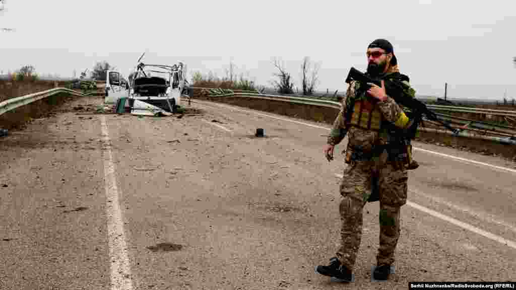Őrt álló ukrán fegyveres és egy megsemmisített kocsi a Herszonba vezető úton