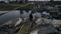 O femeie traversează un pod dărâmat din Bakhmut, regiunea Donețk, Ucraina, imafina făcută pe 11 noiembrie 2022. (AP Photo/LIBKOS) 