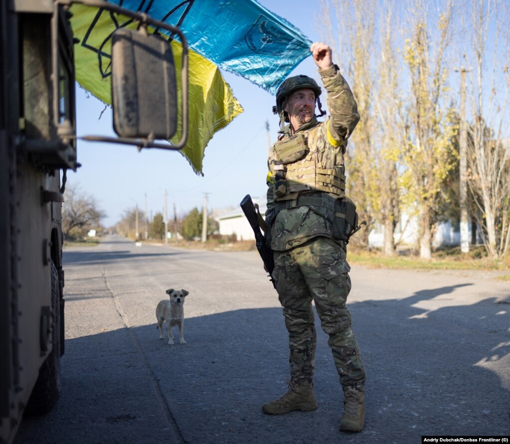 Një ushtar mban një flamur ukrainas të grisur ndërsa dielli po perëndon në qytetin e sapomarrë. Snihurivka ishte pushtuar nga forcat ruse që nga marsi