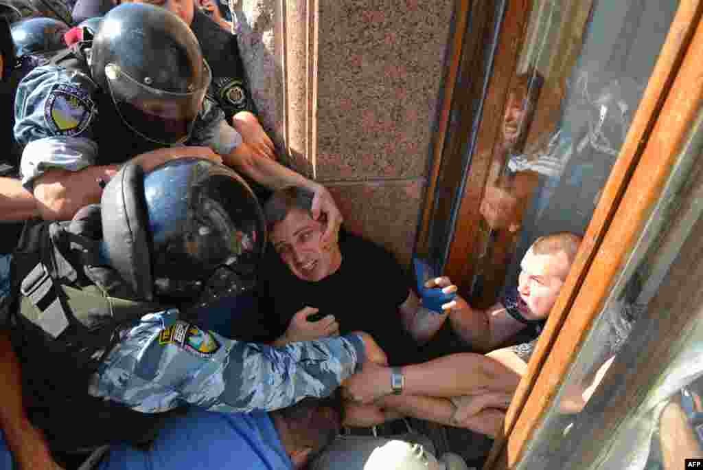 Ukrainian riot police officers stop an opposition deputy as he tries to enter the building of the Kyiv City Council through a window. The opposition lawmakers have been blocking council sessions for months, demanding that elections for the Kyiv City Council and the Kyiv mayor&#39;s office be held this year. (AFP/Vitali Lazebnyk)