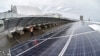 Workers install equipment at the new solar power plant in Chernobyl in December 2017, with the New Safe Confinement over the fourth block of the nuclear plant in the background.