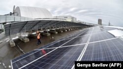 Workers install equipment at the new solar power plant in Chernobyl in December 2017, with the New Safe Confinement over the fourth block of the nuclear plant in the background.