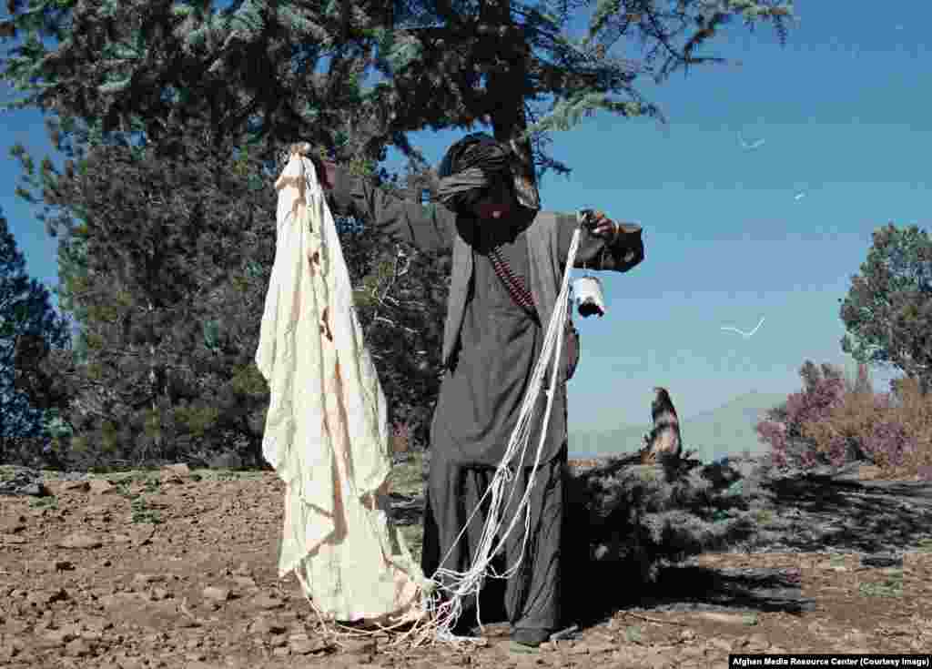 A mujahedin fighter holds the remains of a parachute bomb. The design allows ground-attack jets to drop bombs at low altitude without being caught up by the explosion.