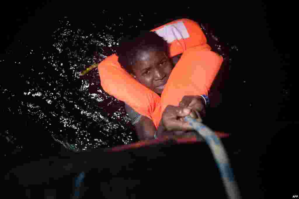 A young migrant holds onto a rope during a rescue operation off Libya&#39;s Mediterranean coastline on October 12. (AFP/Aris Messinis)