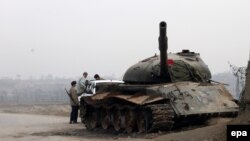 Members of the Afghan security forces stand guard near a tank that was burned by Taliban militants in the Chardara district of Kunduz Province.