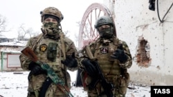 Doi luptători ai grupului de mercenari Wagner, fotografiați lângă clădiri distruse în timpul luptelor, Soledar, Ucraina.