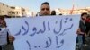 مردی در تظاهرات روز ۲۵ ژانویه در مقابل بانک مرکزی عراق نوشته‌ای در دست گرفته که روی آن نوشته شده است: «نرخ دلار را کاهش دهید وگرنه...!»