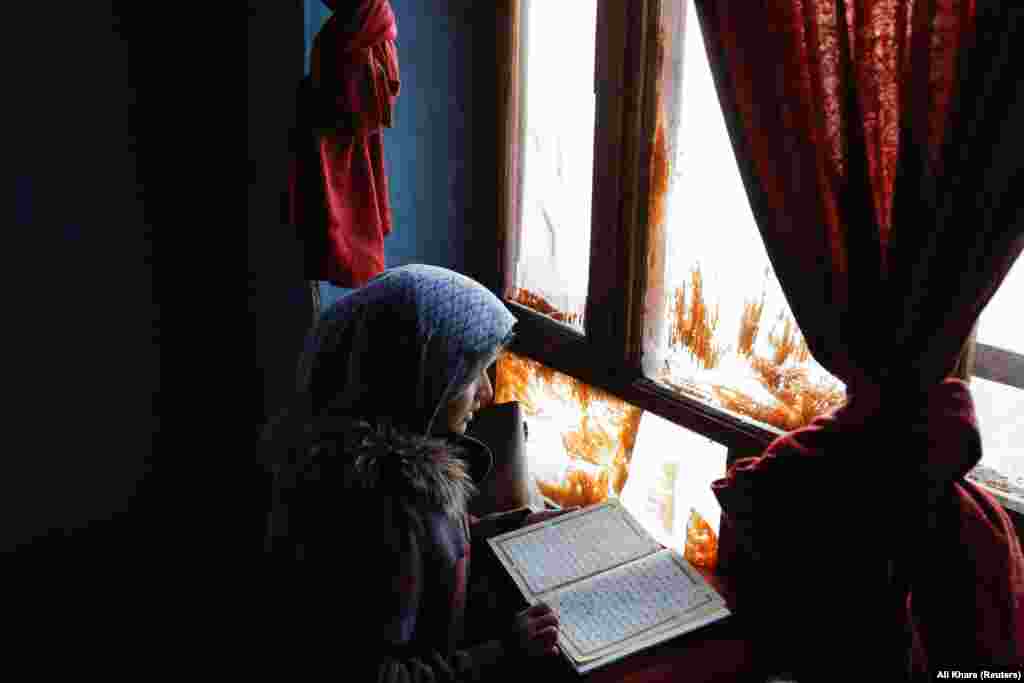 One of Amrullah&#39;s sisters reads the Koran as light filters through the dirty windowpanes.