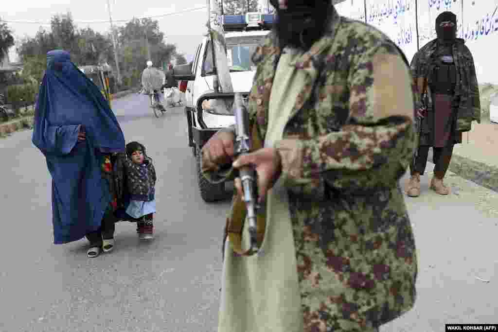 A woman wearing a burqa and a child walk past Taliban fighters along a roadside in Jalalabad, Afghanistan.