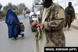 A woman and a child walk past Taliban fighters along a roadside in Jalalabad.