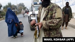 A woman wearing a burqa and a child walk past Taliban fighters along a roadside in Jalalabad, Afghanistan. (file photo)