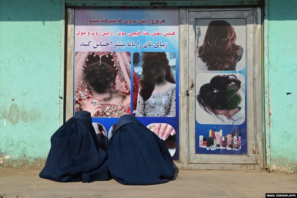 Dy gra afgane, të veshura me burka, duke qëndruar ulur, para një salloni bukurie, ku imazhet e grave ishin përdhosur me ngjyrë, në Xhalalabad, Afganistan, më 13 dhjetor.