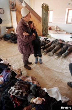 Етнічний албанець обіймає хлопчика серед тіл убитих жителів села Рачак, знайдених у рові на півдні Косов. 18 січня 1999 року. Звинувачення проти колишнього президента Югославії Слободана Мілошевича стосувалися зокрема й вигнання сотень тисяч косовських албанців із їхніх домівок у 1999 році, а також конкретних масових вбивств у таких селах, як Рачак, Бела Црква та Велика Круша.