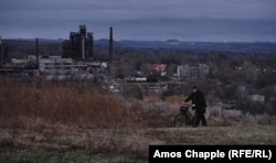 A man walks his bicycle along a hilltop pathway above New York. The lights in the background are of Horlivka, a town controlled by Kremlin-backed separatists. New York's phenol factory is on left.