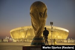 Un bărbat privește stadionul Lusail, unde pe 18 decembrie se va disputa finala Cupei Mondiale din Qatar, lângă o replică uriașă a trofeului.