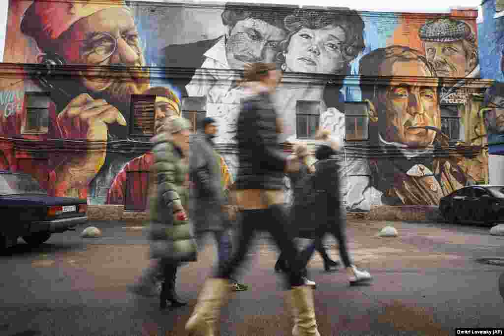 People walk past a mural depicting the characters of famous Soviet films on the building of the Lenfilm film company in St. Petersburg, Russia.