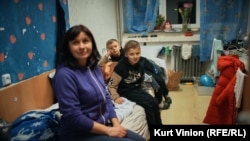 Олга Хришанович седи на леглото с близнаците си в малката им стая в общежитието. Те не знаят къде ще живеят след март.