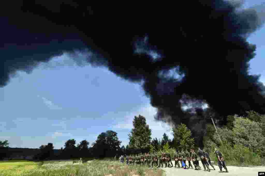 Dark smoke billows from a fire at a fuel depot as Ukrainian servicemen walk past in the village of Kryachki, some 30 kilometers southwest of Kyiv. The blaze killed five people, including three firemen. (AFP/Sergei Supinsky)
