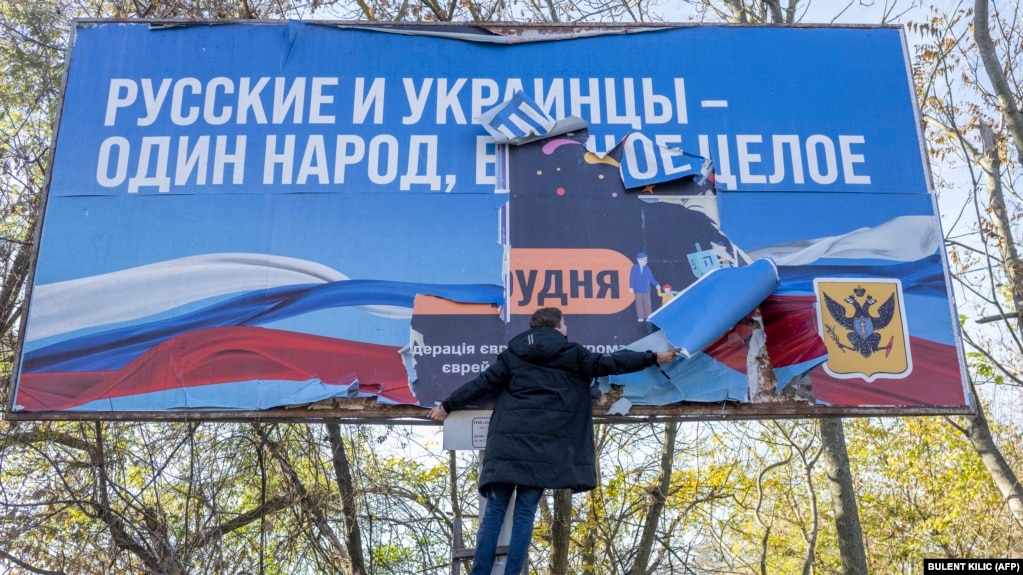Мужчина снимает транспарант периода российской оккупации «Русские и украинцы — один народ, одно целое» в недавно освобожденном Херсоне, 14 ноября 2022 года