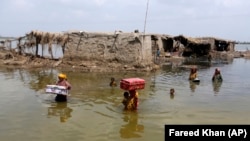 Жените носат предмети спасени од нивниот поплавен дом по монсунските дождови во провинцијата Синд, во Пакистан во септември 2022 година. Повеќе од 1.300 луѓе загинаа, а милиони ги загубија своите домови во поплавите предизвикани од невообичаено обилните монсунски дождови за кои многу експерти ги обвинија климатските промени.