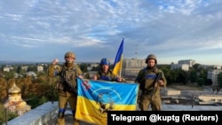 Soldați ucraineni arborează steagul pe acoperișul unei clădiri din Kupiansk, 10 septembrie 2022.