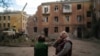 Raisa Smielkova, 75 de ani, privește pompierii care lucrează pentru a stinge un incendiu la o clădire rezidențială din Sloviansk, Ucraina, miercuri, 7 septembrie 2022. Smielkova dormea în momentul exploziei. „Ai fi un prost să nu te sperii de asta”, spune ea. 