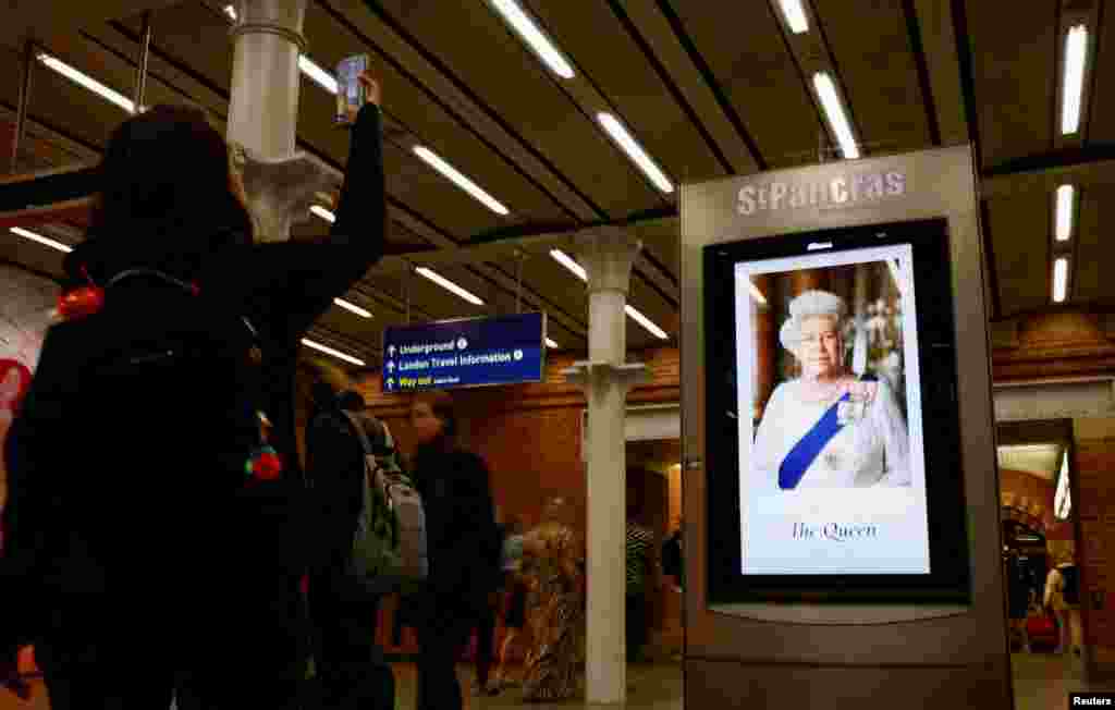 Një grua bën një fotografi derisa njerëzit ecin pranë imazhit të Mbretëreshës Elizabeth II në stacionin Pancras në Londër, pas vdekjes së saj. 9 shtator 2022.&nbsp;