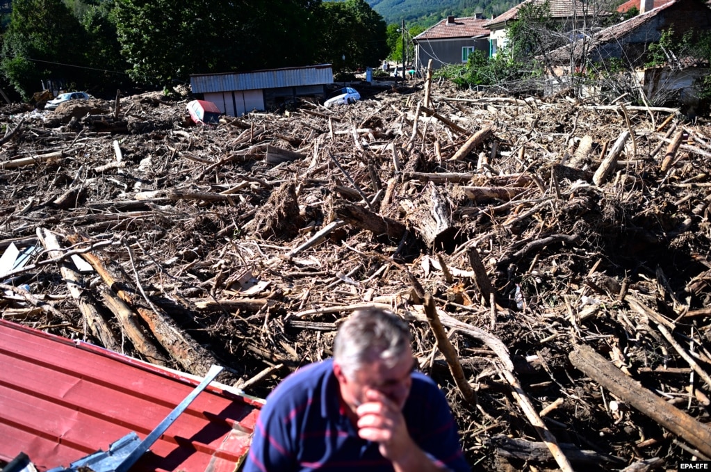 Një burrë shihet ulur pranë një grumbulli drunjsh të pemëve të bartura nga uji që hyn pas përmbytjeve të mëdha në fshatin Sllatinë, Bullgari.