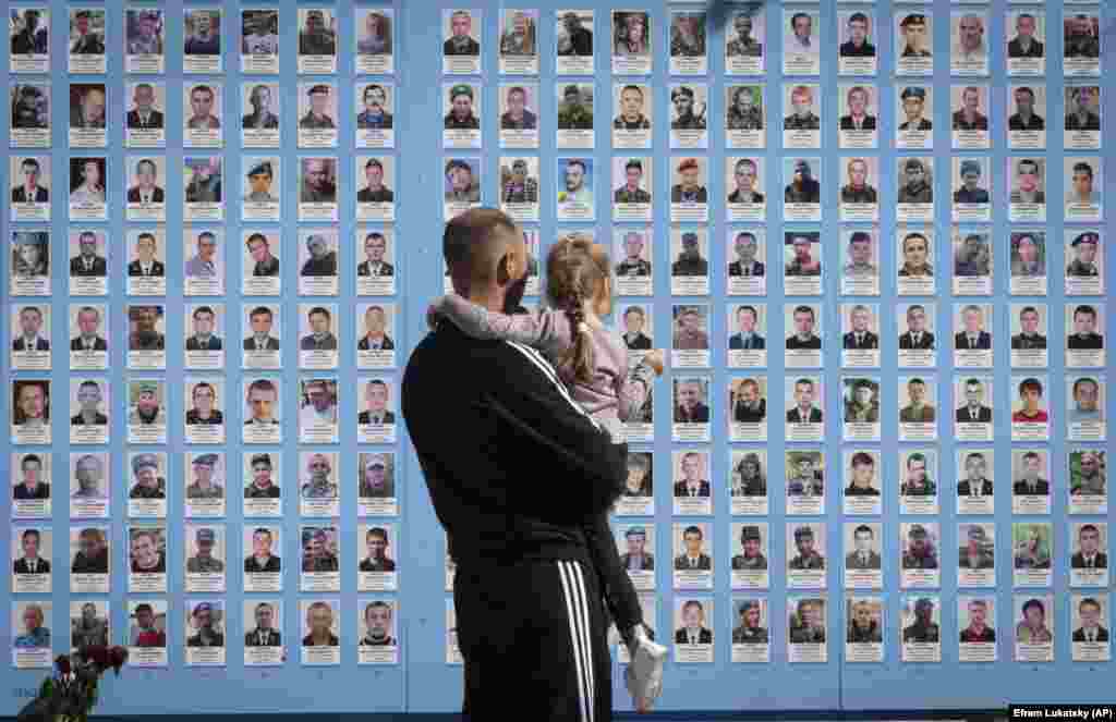 A man in Kyiv holds his child at the Memorial Wall for Fallen Defenders of Ukraine, showing her photos of his fellow soldiers who have been killed in his country&#39;s fight against invading Russian forces.&nbsp;