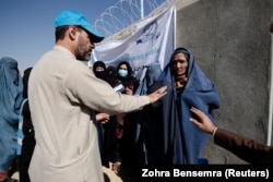 A UNHCR worker explains aid collection procedures to displaced Afghan women on the outskirts of Kabul. (file photo)