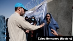 A UNHCR worker explains aid collection procedures to displaced Afghan women outside a distribution center on the outskirts of Kabul on October 28.