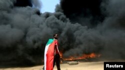 Čovek sa zastavom Sudana stoji ispred zapaljene gomile guma tokom protesta u Kartumu, Sudan, 21. oktobra 2021. 