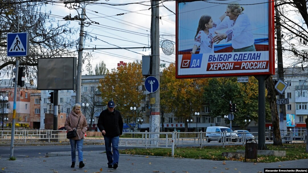 Люди идут по улице рядом с транспарантом с надписью «Выбор сделан. Херсон – это Россия» накануне освобождение города украинскими войсками, 31 октября 2022 года