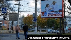 Люди идут по улице рядом с транспарантом с надписью «Выбор сделан. Херсон – это Россия» накануне освобождение города украинскими войсками, 31 октября 2022 года