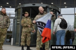 Мужчины перед входом в "ЧВК Вагнер Центр" разворачивают флаг