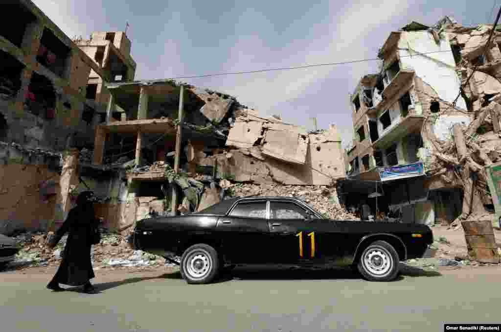 Жінка проходить повз автомобіль, припаркований біля пошкоджених будівель у Думі, у східному передмісті Дамаска, Сирія, 9 березня 2021 року. Збройний конфлікт у Сирії триває 10 років, за цей час загинуло понад 350 тисяч людей