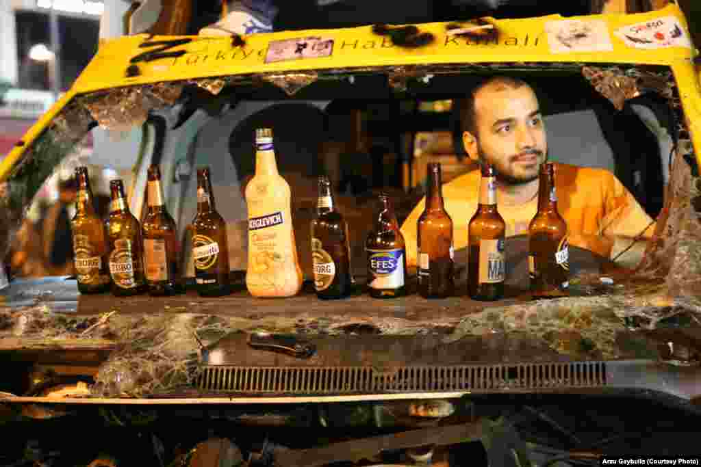 A Turkish football fan relaxes in a burned-out minibus during antigovernment protests in Istanbul&#39;s Taksim Square. Beer is a hot commodity in the square, where many protesters are angry that Turkish Prime Minister Recep Tayyip Erdogan has tried to restrict alcohol sales. (Arzu Geybulla for RFE/RL)