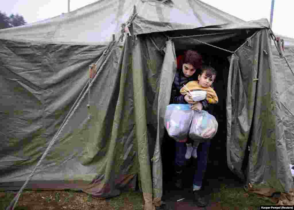 A migrant woman carries a child as they exit a tent outside a transport and logistics center near the Polish border in Belarus&#39;s Hrodna region.