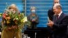 Cancelarul actual al Germaniei, Angela Merkel, primește un buchet de flori de la ministrul german de Finanțe și viitor cancelar al țării, Olaf Scholz, înainte de reuniunea săptămânală a cabinetului acesteia. Fotografie realizată în Berlin, Germania, pe 24 noiembrie 2021.