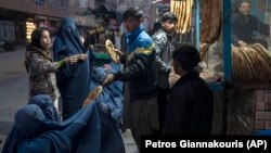 A man distributes bread to burqa-wearing Afghan women outside a bakery in Kabul.