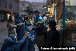 A man distributes bread to Afghan women outside a bakery in Kabul.